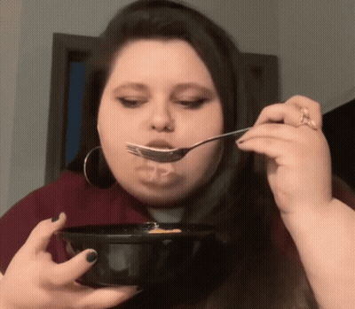 A Woman Is Eating From A Bowl With A Fork . GIF