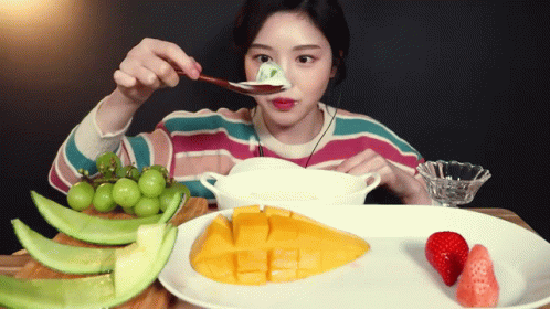 A Woman Is Eating Fruit With A Spoon And A Bowl GIF