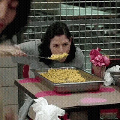 A Woman Is Eating Macaroni And Cheese With A Spoon In Her Mouth GIF