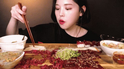 A Woman Is Eating Meat With Chopsticks While Wearing Ear Buds GIF
