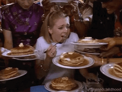 A Woman Is Eating Pancakes With A Fork While A Group Of People Are Holding Plates Of Pancakes . GIF