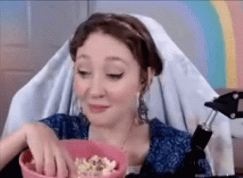 A Woman Is Eating Popcorn While Sitting In A Chair . GIF