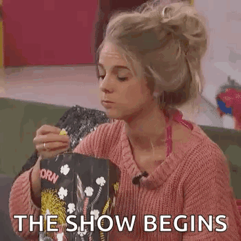 A Woman Is Eating Popcorn While Sitting On A Couch And Says `` The Show Begins '' . GIF