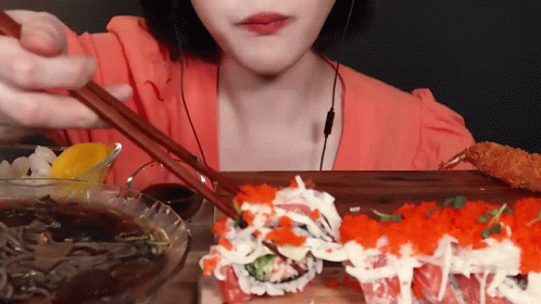 A Woman Is Eating Sushi With Chopsticks While Wearing Ear Buds GIF