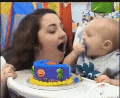 A Woman Is Feeding A Baby A Birthday Cake With A Frog On It . GIF