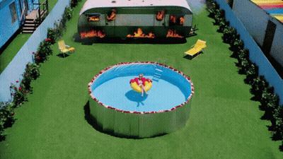 A Woman Is Floating In A Swimming Pool In Front Of A Trailer That Is On Fire GIF