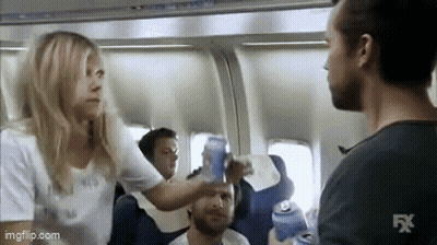 A Woman Is Giving A Man A Beer On An Airplane . GIF