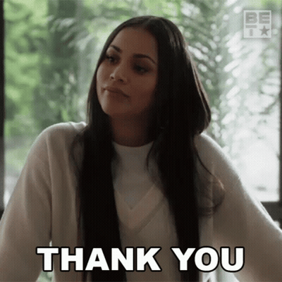 A Woman Is Giving A Thank You Gesture While Sitting In Front Of A Window . GIF