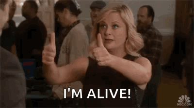 A Woman Is Giving A Thumbs Up And Saying `` I 'M Alive '' In A Crowded Room . GIF