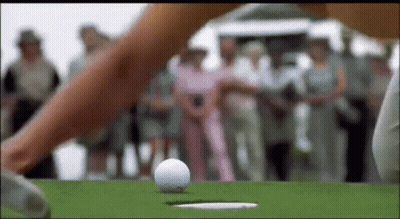 A Woman Is Hitting A Golf Ball Into A Hole . GIF