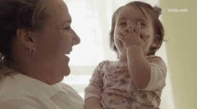 A Woman Is Holding A Baby Girl In Her Arms And The Baby Is Covering Her Face With Her Hands . GIF