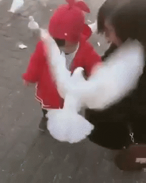 A Woman Is Holding A Baby In Her Arms And A Pigeon Is Flying Away From Her . GIF