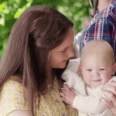 A Woman Is Holding A Baby In Her Arms And The Baby Is Smiling For The Camera . GIF
