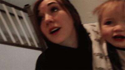 A Woman Is Holding A Baby In Her Arms And The Baby Is Wearing A Dinosaur Shirt GIF