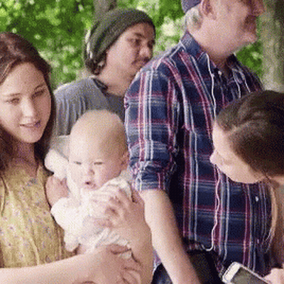A Woman Is Holding A Baby In Her Arms While A Man Looks At His Phone GIF
