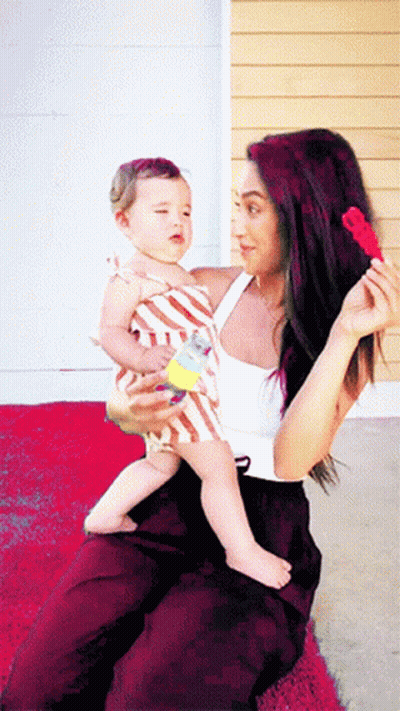 A Woman Is Holding A Baby In Her Lap And Holding A Toy In Her Hand GIF