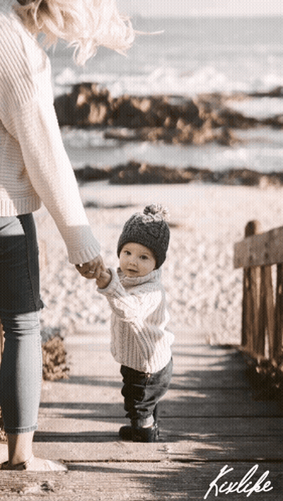 A Woman Is Holding A Baby 'S Hand While They Walk On A Boardwalk GIF
