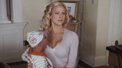 A Woman Is Holding A Baby Wearing A Hat With A Swirl On It GIF