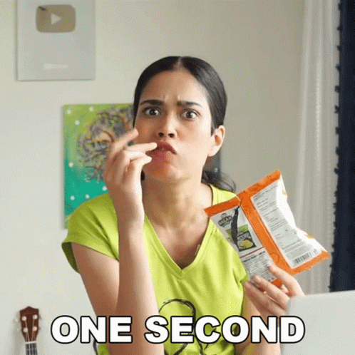 A Woman Is Holding A Bag Of Chips And The Words One Second Are Above Her GIF