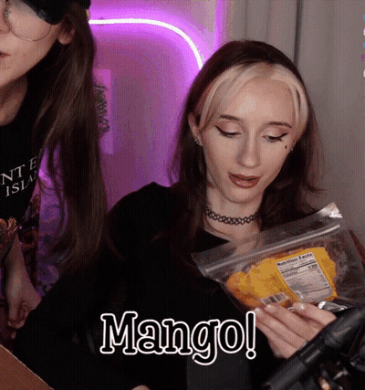A Woman Is Holding A Bag Of Mango Chips In Her Hands GIF