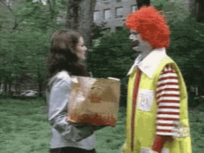 A Woman Is Holding A Bag Of Mcdonald 'S French Fries And Talking To A Clown . GIF
