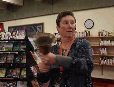 A Woman Is Holding A Bell In Front Of A Book Shelf That Has A Book Called Ross On It GIF