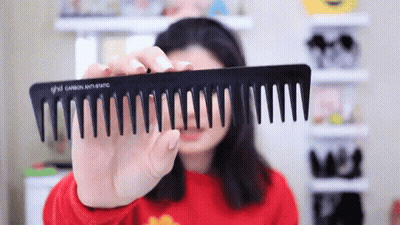 A Woman Is Holding A Black Comb That Says Ghd GIF