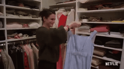A Woman Is Holding A Blue Dress In A Closet Filled With Clothes . GIF