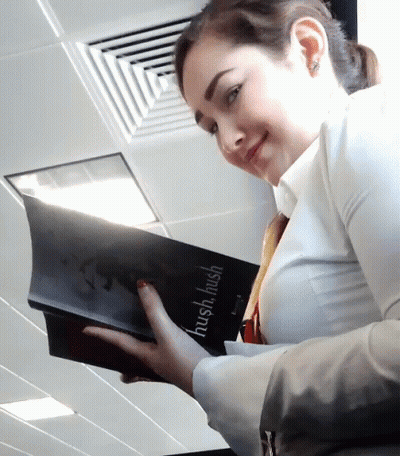A Woman Is Holding A Book That Says Hush Hush On It GIF