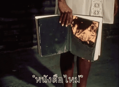 A Woman Is Holding A Book With A Piece Of Gold Foil On It . GIF