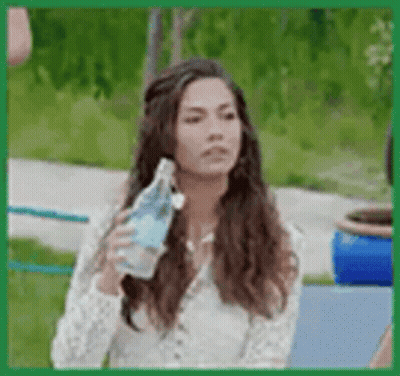 A Woman Is Holding A Bottle Of Water In Her Hand While Sitting On A Bench . GIF