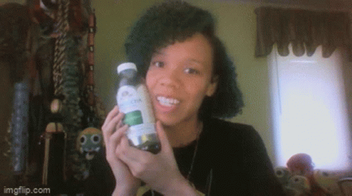 A Woman Is Holding A Bottle With A Green Label And Smiling GIF