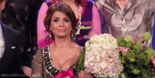 A Woman Is Holding A Bouquet Of Flowers In Her Hands While Sitting In A Crowd . GIF