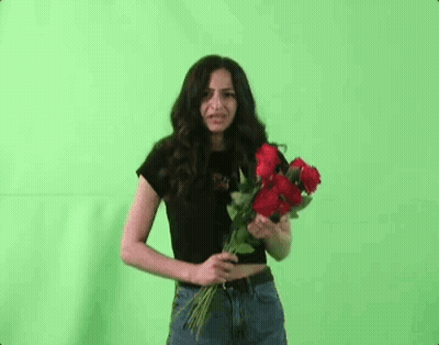 A Woman Is Holding A Bouquet Of Red Roses In Front Of Her Face Against A Green Screen . GIF