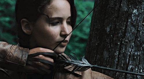 A Woman Is Holding A Bow And Arrow With A Feather In Her Mouth GIF