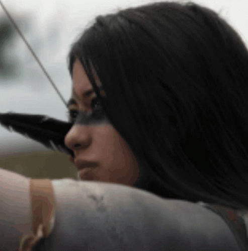 A Woman Is Holding A Bow And Arrow With A Feather On Her Face . GIF