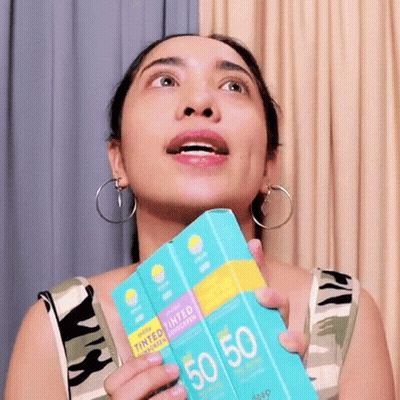 A Woman Is Holding A Box Of Tinted Sunscreen In Her Hand . GIF