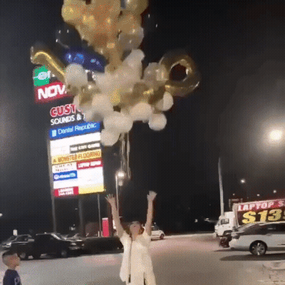 A Woman Is Holding A Bunch Of Balloons In Front Of A Building That Says Gusto Sounds GIF