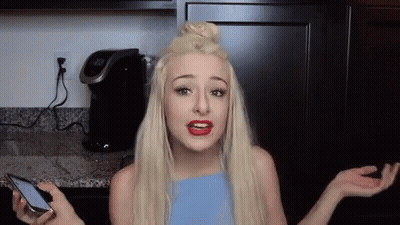 A Woman Is Holding A Cell Phone And Making A Funny Face In A Kitchen . GIF