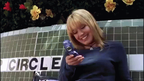 A Woman Is Holding A Cell Phone In Front Of A Circle Sign GIF