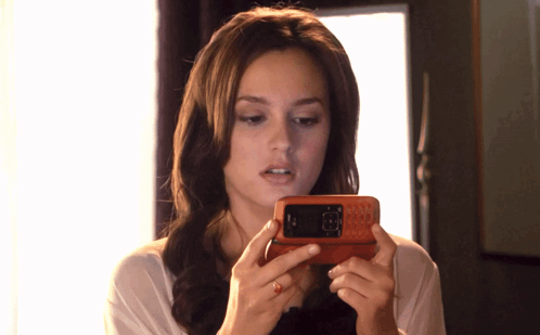 A Woman Is Holding A Cell Phone In Her Hands And Looking At The Screen GIF