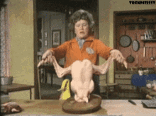 A Woman Is Holding A Dead Chicken Over A Cutting Board GIF