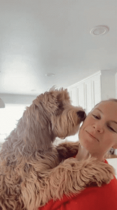 A Woman Is Holding A Dog In Her Arms And The Dog Is Sniffing The Woman 'S Face GIF