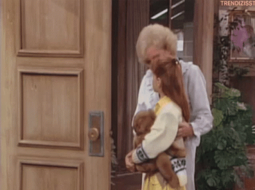 A Woman Is Holding A Doll And A Teddy Bear While Standing In Front Of A Wooden Door . GIF