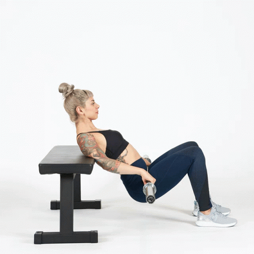 A Woman Is Holding A Dumbbell While Laying On A Bench GIF