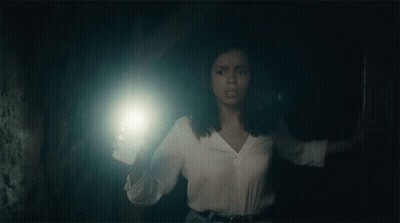 A Woman Is Holding A Flashlight In Her Hand In A Dark Room . GIF