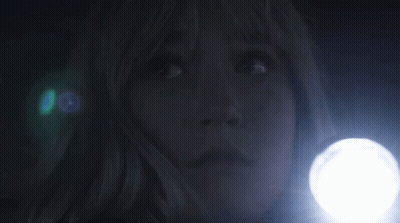 A Woman Is Holding A Flashlight In The Dark And Looking Up . GIF