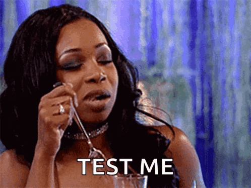 A Woman Is Holding A Fork In Her Mouth And Saying Test Me . GIF