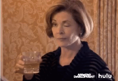 A Woman Is Holding A Glass Of Beer In Front Of A Wall That Says Arrested Development . GIF