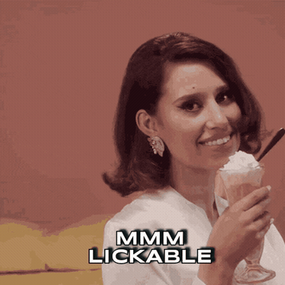 A Woman Is Holding A Glass Of Milkshake With Whipped Cream And The Words Mmmm Lickable Below Her GIF